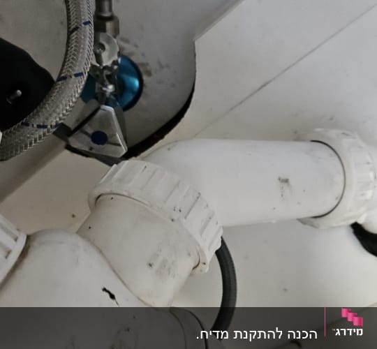צינור פלסטיק לבן עם חיבורים מתכתיים מתחת לכיור